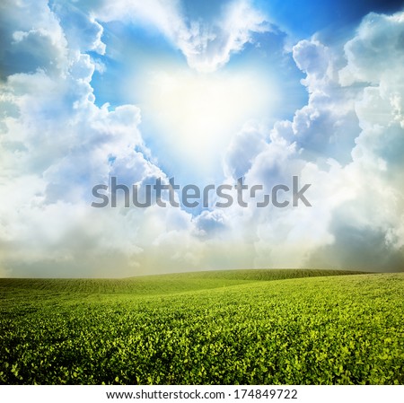 Green meadow under blue sky with heart clouds