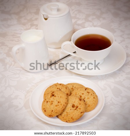 A cup of tea with cookies,milk jug and sugar bowl