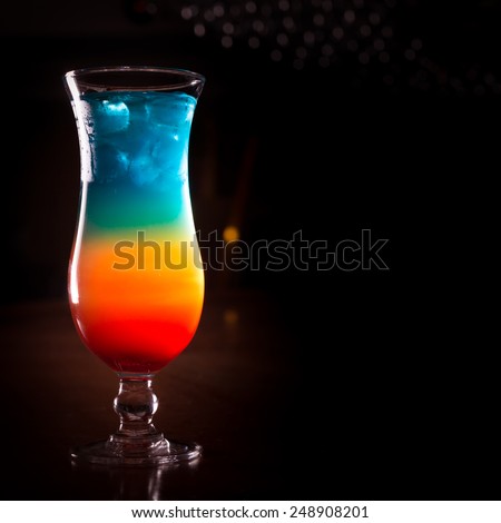 Rainbow cocktail on the bar stand with dark background. Shallow DOF and marsala tonned