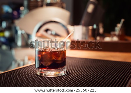 Black russian cocktail on the bar stand on rubber mat. Shallow DOF and marsala tonned