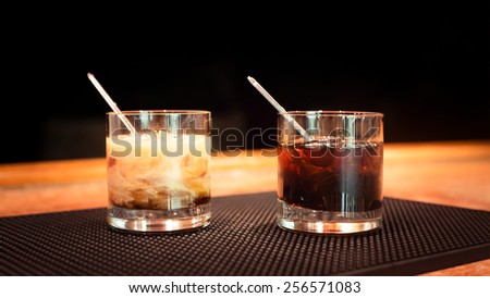 Black russian and white russian cocktails on the bar stand on rubber mat. Shallow DOF and marsala tonned