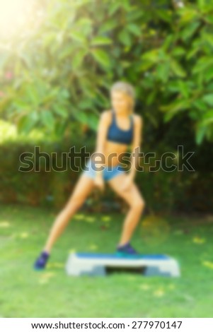 Young woman during her outdoor step workout. Abstract blur background with bokeh, lightly toned