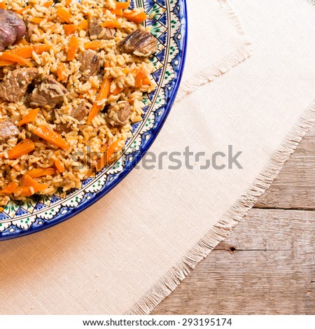 Pilaf in the handmade plate on the wooden background. Square