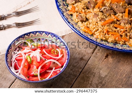 Pilaf and achichuk salad in handmade plate with antique forks on wooden background. Horizontal