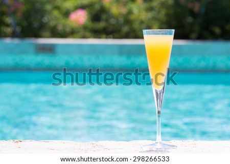 Glass of Bellini cocktail on the pool nosing at the tropical resort. Horizontal, cocktail on right side