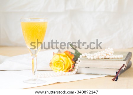 Glass of mimosa cocktail with vintage books and pearls. Lightweight background. Vintage style. Horizontal