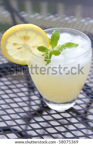 Top view of a cup of lemonade with a slice of lemon, sprig of mint and crushed ice.