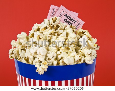 A popcorn bucket over a red background. Movie stubs sitting over the popcorn.
