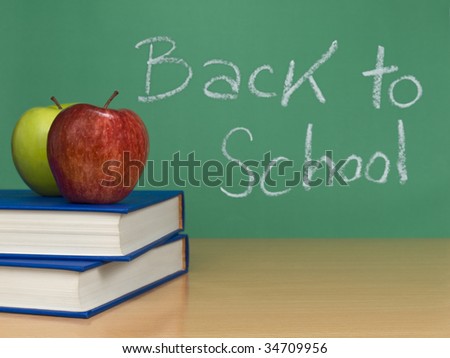 Back to school written on a chalkboard. Two apples over books on the foreground.