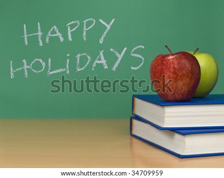 Happy holidays written on a chalkboard. Two apples over books on the foreground.