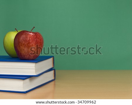 A blank chalkboard with two apples over books.