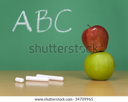 ABC written on a chalkboard. Some chalks and a red apple over a green one on the foreground.