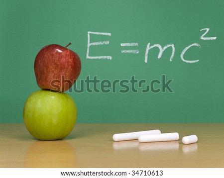 Einsteins formula of theory of relativity on a chalkboard. Some chalks and apples on the foreground.