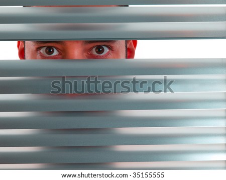 A red man looks to the camera through the blinds.