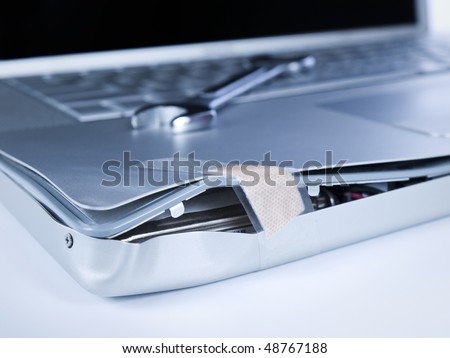 A band aid is fixing a damaged laptop. A spanner is over the computer.