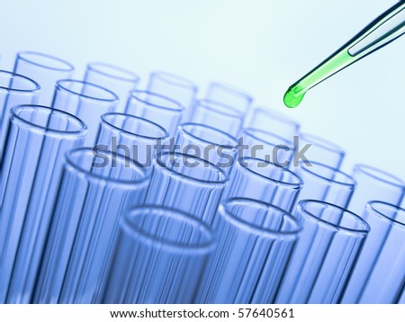 Close up of a pipette dropping a green sample into a test tube.