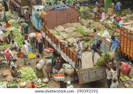 BANGALORE, INDIA - May 27, 2014: Laborers empty out sacks from a truck carrying produce, vendors sell vegetables below