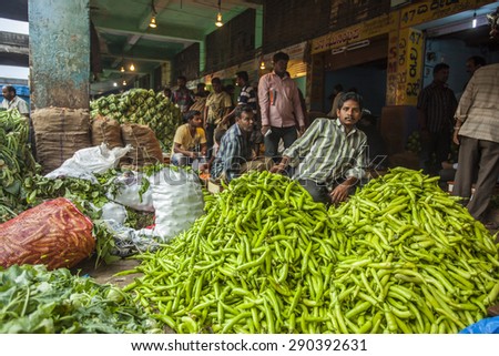 BANGALORE, INDIA - May 13, 2014: a vegetable vendor sells fresh green chillies at his stall in the busy city market, other vendors in the background