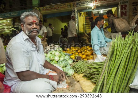 BANGALORE, INDIA - May 13, 2014: an old vegetable vendor sells drumstick at his stall in the busy city market, other vendors in the background
