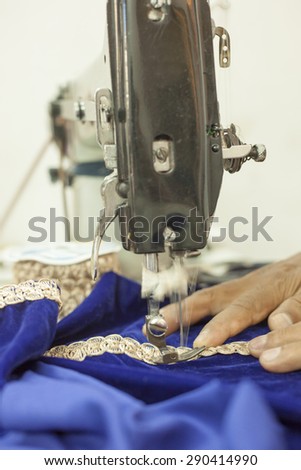 Bangalore, Karnataka, India - March 20, 2014: An unidentified traditional tailor stitches gold embroidered onto a cloth using a sewign machine.