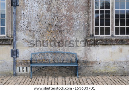 empty antique bench against an old wall with a leaded window