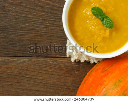 Pumpkin soup in a cup placed on a wooden table.