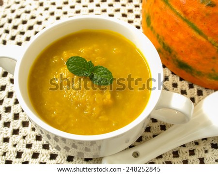 Pumpkin soup in a cup placed on a wooden table.