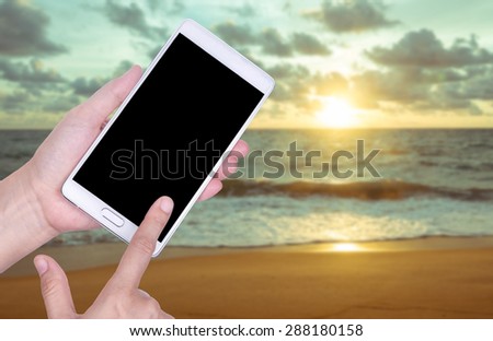 Human hand hold and touch screen smart phone, tablet,cellphone on blurred beach background.
