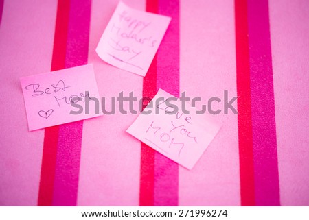 Appreciation message to Happy Mother\'s Day on pink sticky notes  Best Mom, Love you Mom handwritten text on paper, red magenta fuchsia striped background. Shallow depth of field, blurred