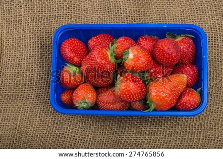 Aerial view fresh aromatic strawberries in blue supermarket plastic tray 
Closeup of Healthy low carb and low fat food fruits for diet or sweet dessert from farmers market against jute sack background