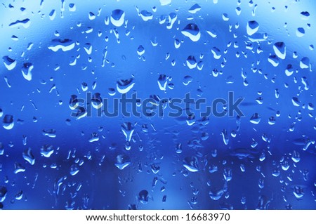 Rain drops on a glass window with a blue tint