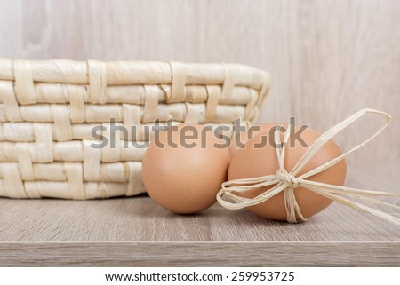 Decorated fresh eggs next to the woven basket on a wooden background