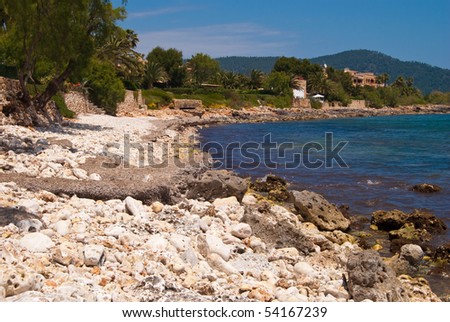 White pebble on the beach of Mediterranean Sea. Hotels and residential area in Cala Bona suburbs, Majorca island, Spain