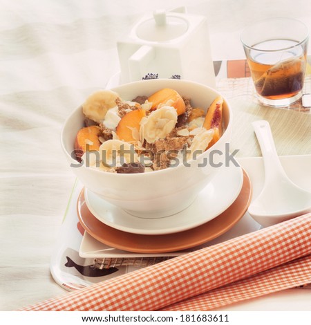 Breakfast in bed tray cereal, peach and banana, yogurt and tea, warm orange color. Square image