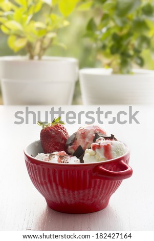 red bowl with ice cream, three scoops of vanilla and strawberry. Outdoor. daylight