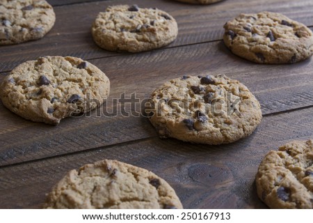 Freshly baked chocolate chip cookies on wooden table to cool, with soft focus in the background