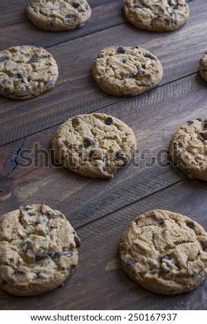 Freshly baked chocolate chip cookies on wooden table to cool, with soft focus in the background