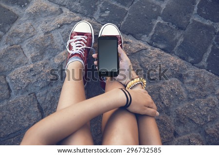 teenager girl sitting with mobile phone in hand, in ancient stone floor