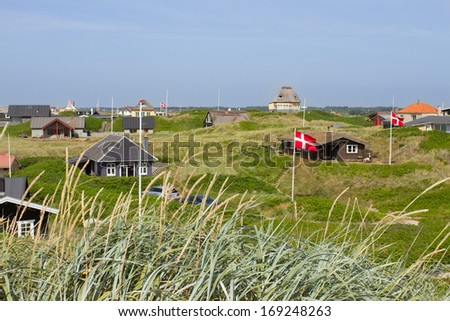 Danish holiday houses scattered among the sand dunes at the North Sea coastline in Soendervig, Denmark. Picture taken on a sunny summer day. Danish flags are visible on the picture.