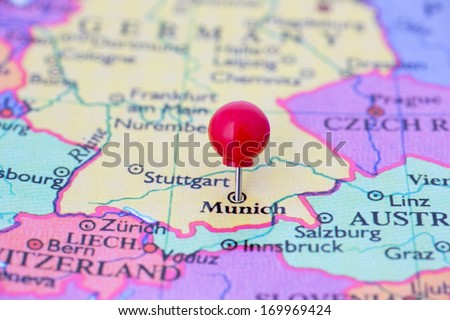Round red thumb tack pinched through city of Munich on Germany map. Part of collection covering many cities and capitals of Europe.