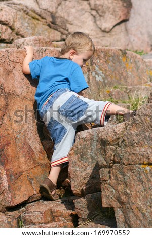 Boy toddler climbing up a large rock.