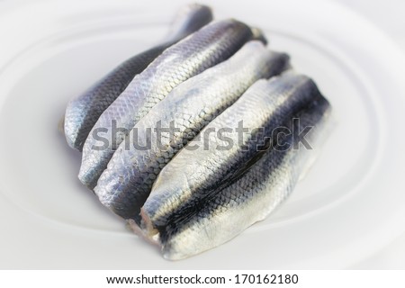 Four raw herring fish lying on white plate ready for cooking