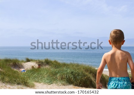 Young boy is having a panoramic view of the entire horizon over water at the North Sea shore in Western Jutland, Denmark. Plenty of copy space.
