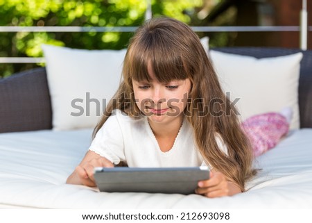 Caucasian girl playing with her tablet outdoors on the patio during summer time.