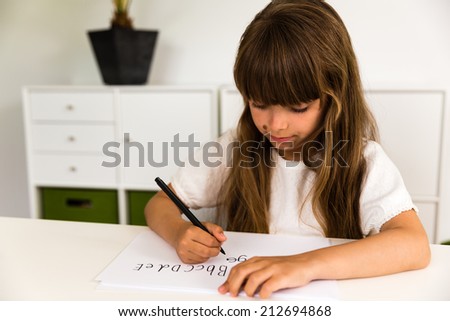 Young caucasian girl with long hair writing letters on a white piece of paper.