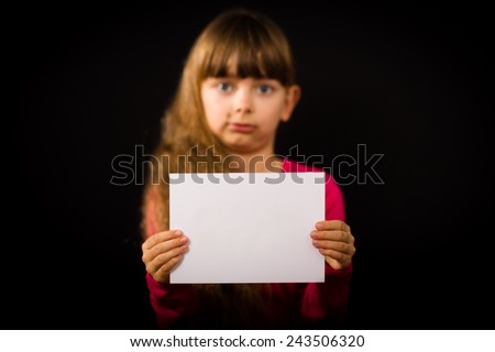 Studio shot of sad girl holding a sign made of white paper. Focus on paper. Girl is blurred.