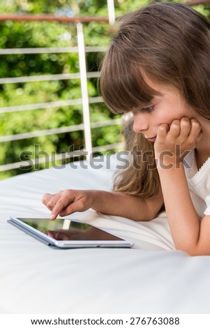 Caucasian girl playing with her tablet outdoors on the patio during summer time.