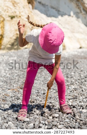 Girl pecking at rocks with her hammer on a sunny summer day.
