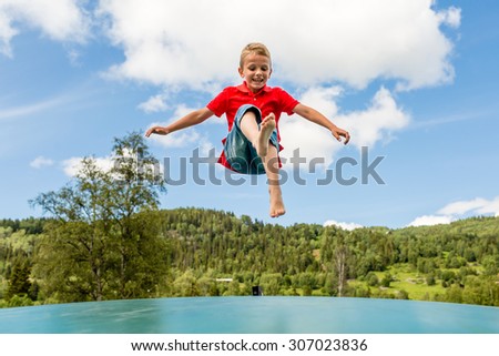 Young Scandinavian boy playing and having fun while jumping up and down on inflatable bouncing trampoline.