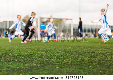 Shallow depth of field shot of young boys playing a kids football match on green turf.